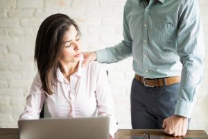 stock photo of woman sitting at a laptop recoiling as she is touch on the shoulder by a man whose face is out of shot