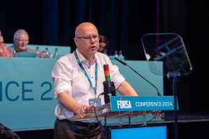Kevinin Callinan standing at a podium, speaking at Biennial Conference 2024