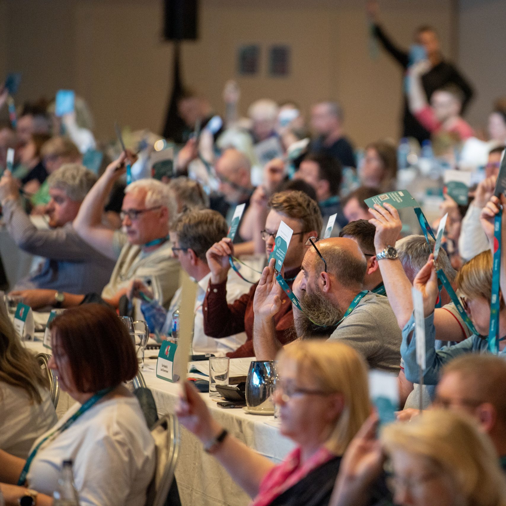Forsa members at conference holding up their hands and badges to vote on motions.