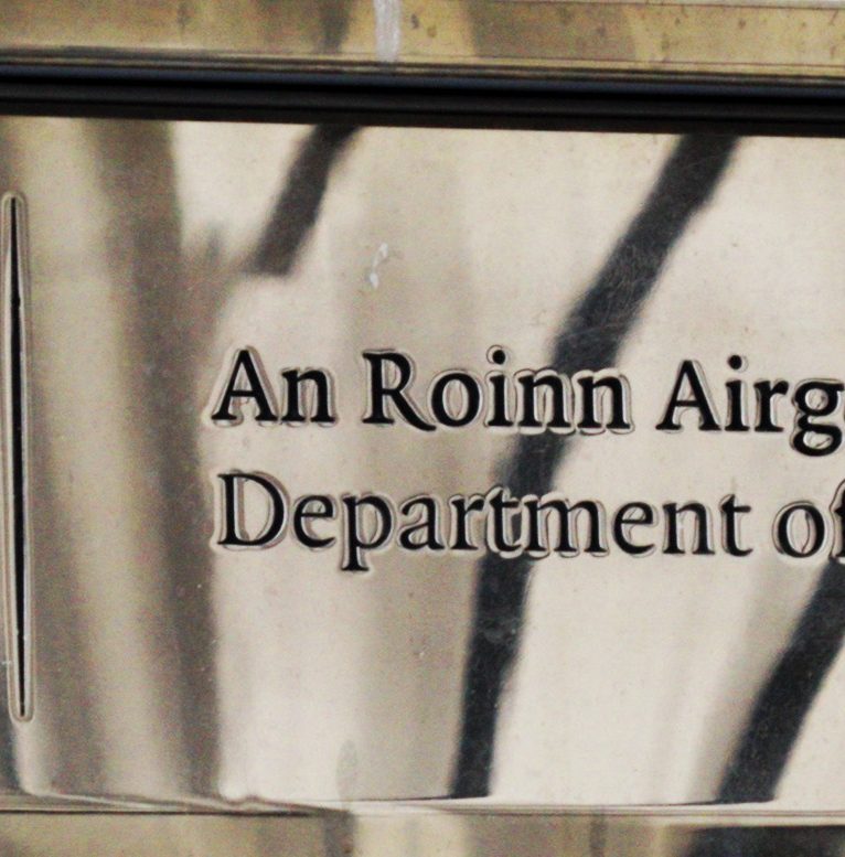A photograph of a government department brass plaque. The image cuts off the latter half of plaque so the department will forever remain a mystery, unless you read the irish, can see "airg" and figure out it's the start of "airgeadais."