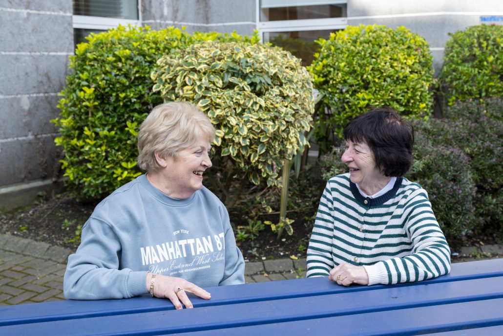 Two women sitting at a blue bench outdoors, chatting with each other, outside the Fórsa retired members meeting
