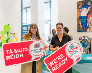 Two women holding signs for "we're ready week" ahead of industrial action. One sign reads "we're ready" the other is in Irish and reads "Tá muid réidh."